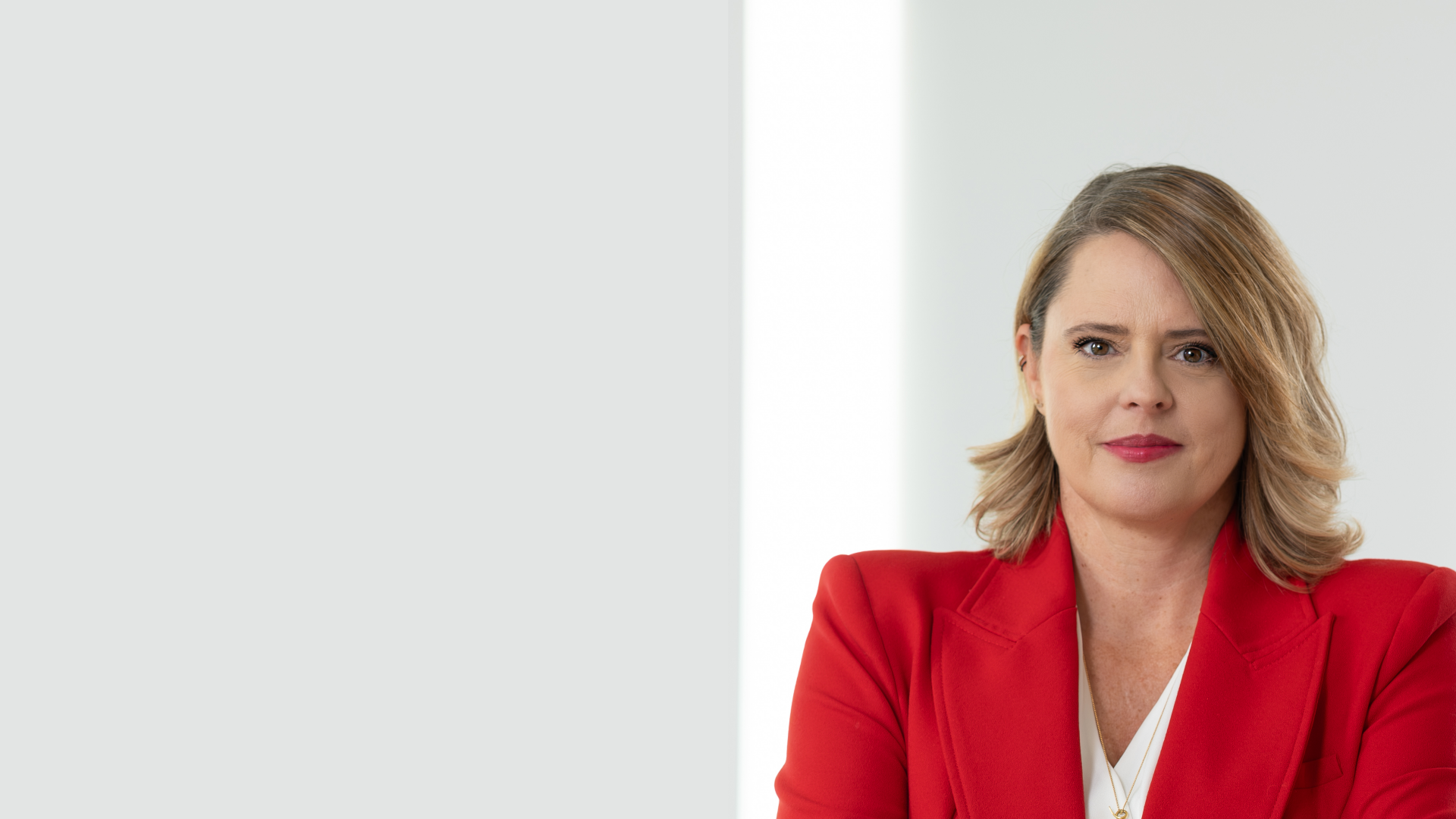 Die Person trägt ein rotes Jackett über einem weißen Hemd und ist möglicherweise in einem professionellen Umfeld. Der Hintergrund ist größtenteils unscharf oder neutral gehalten, was darauf hinweist, dass das Foto auf die Person fokussiert ist.